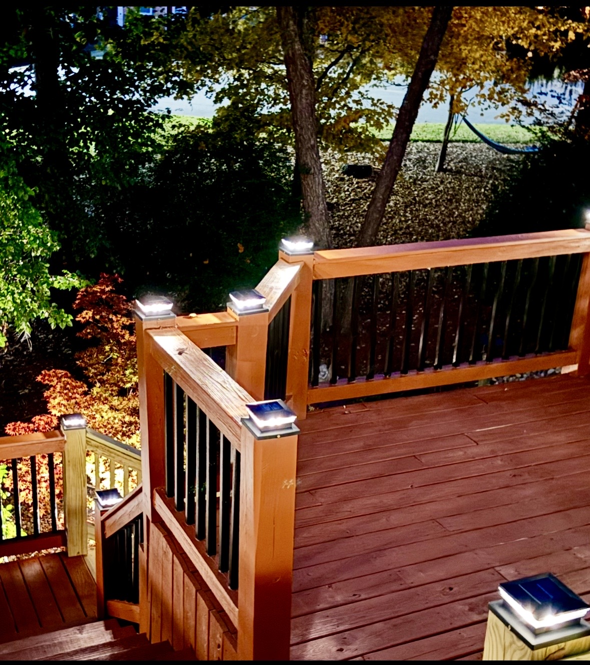 Custom stained wood deck with black balusters, stairs and illuminated post-cap lights at night